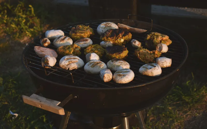 Ein runder Holzkohlegrill mit Champignons und Gemüsebratlingen in der Abendsonne