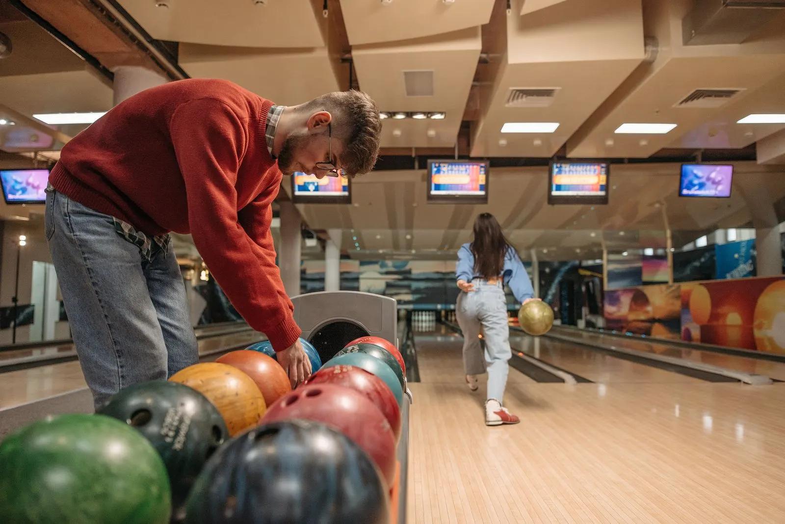 Een man kiest een bowlingbal terwijl zijn vriendin op de baan gooit