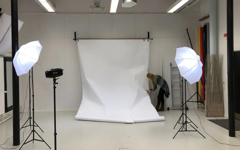 A photo studio with a white paper backdrop and two umbrella lights