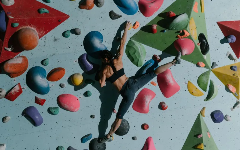 En klättrare hänger i färgglada grepp på en boulderingvägg