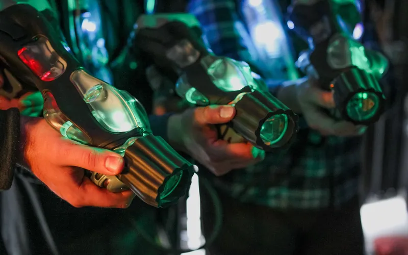 Three players holding glowing laser blasters, ready for a game of laser tag