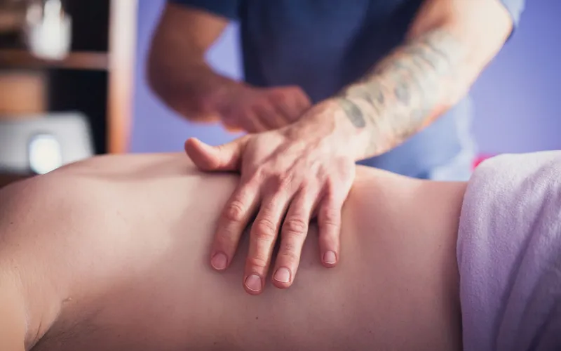 En massör lägger handen på ryggen hos en kund som ligger på massagebänken