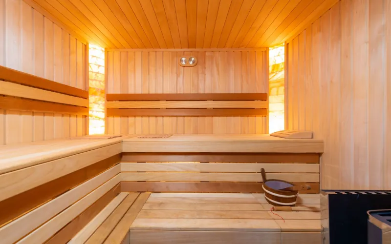 Eine leere Holzsauna mit Bänken auf zwei Ebenen und warmem Licht hinter den Wänden