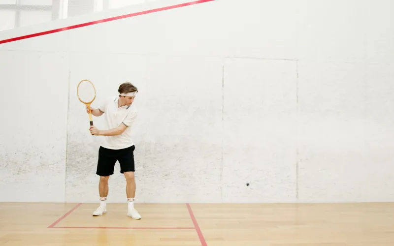 Ein Spieler schlägt eine Rückhand auf einem Squashcourt
